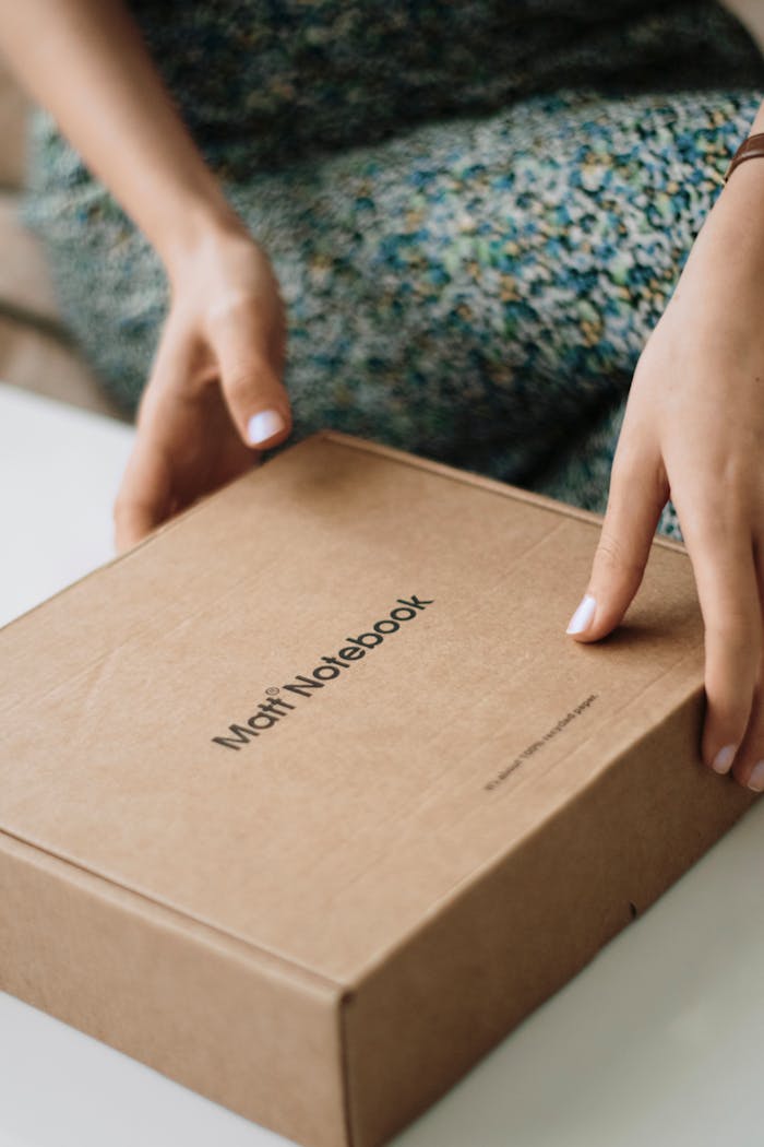 Close-up of hands holding a cardboard box with visible text, indoors.