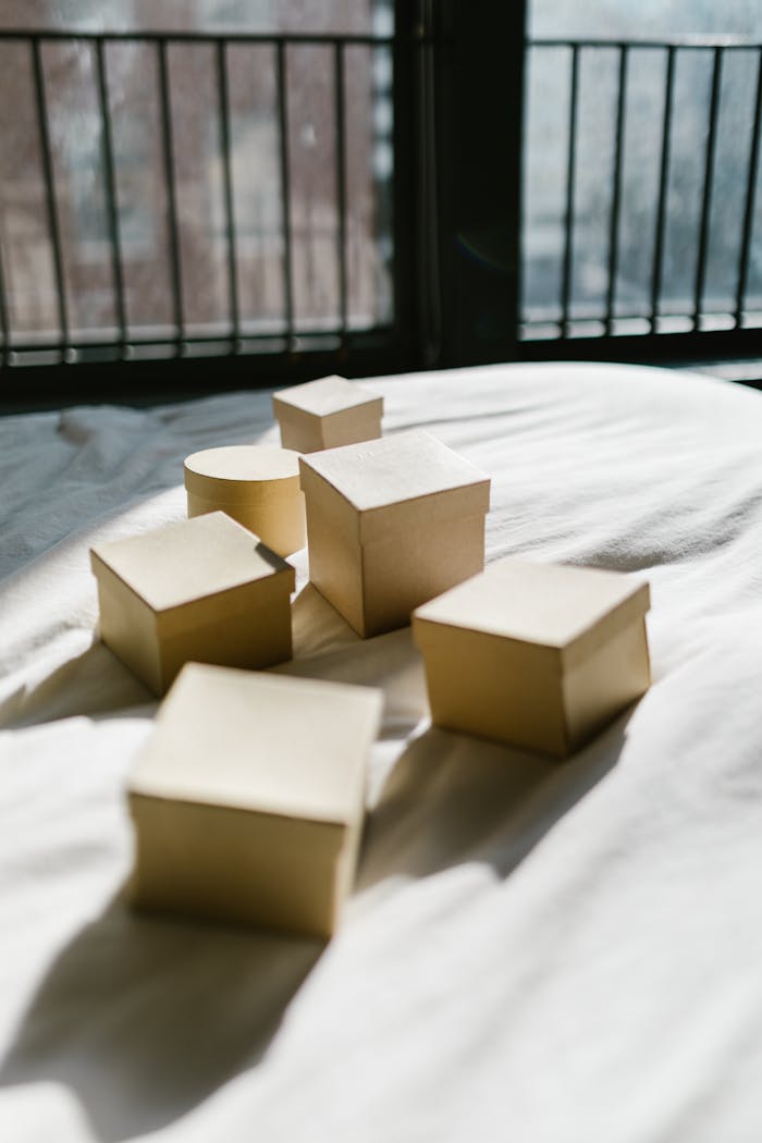 our-experience Sunlit assortments of boxes on a bed with city view in the background, casting intriguing shadows.